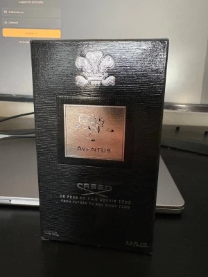 Creed Aventus Eau de Parfum 100ml - Creed Aventus Eau de Parfum i elegant svart kartong med silverdetaljer. Flaskan rymmer 100 ml och doften är känd för sin exklusiva och lyxiga känsla. Förpackningen har en stilren design med Creed-logga och text i silver. Perfekt för dig som vill ha en ikonisk parfym.