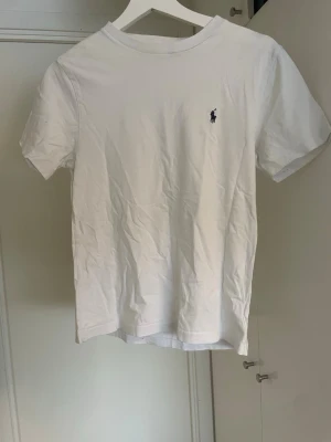 Vit t-shirt från Polo Ralph Lauren - Klassisk vit t-shirt från Polo Ralph Lauren. Tröjan är i ett mycket bra sick. Storlek: 10-12/ 150 cm.