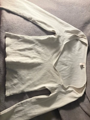 Vit ribbad långärmad topp - Snygg vit ribbad topp med lång ärm och v-ringad hals. Perfekt att styla med jeans eller kjol för en enkel men trendig look. Materialet är mjukt och stretchigt för extra komfort.