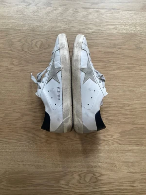 Golden Goose vita sneakers  - Säljer ett par vita Golden Goose sneakers med grå stjärna på sidan och mörkblå häl. Nypris: 5495kr. Skorna har grå skosnören och slitna detaljer för en cool, vintage look. Endast seriösa köpare. Kan sänka pris vid snabb affär! Kvitto finns