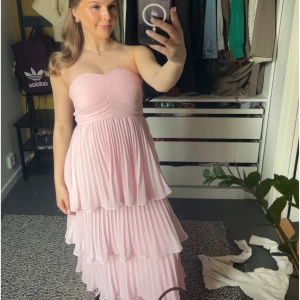 Ljusrosa axelbandslös balklänning - Säljer en ljusrosa långklänning med volanger perfekt för vårens studentbal. Den är ny med prislapp då jag har valt en annan klänning! Storlek 34.