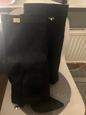 Svarta  stövlar med gulddetalj - Säljer ett par svarta ostövlar i mockaimitation med snygga guldfärgade spännen upptill. Stövlarna har en stilren och hög design som går över knät och passar perfekt till höstens och vinterns outfits.Lululia svarta boots med klack  Strl 40 Helt oanvända  Ny skick  Köpta för 600kr ny pris   Pris går att diskutera  