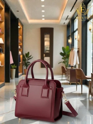 Vinröd handväska med axelrem - Stilren vinröd handväska i fyrkantig modell med både handtag och avtagbar axelrem. Väskan har guldfärgade metalldetaljer och är tillverkad i slätt konstläder. Perfekt för dig som vill ha en trendig accessoar med plats för det viktigaste.