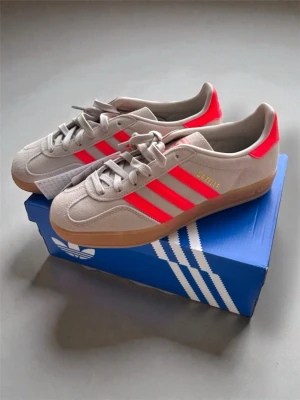 Adidas Gazelle i neonrosa - Adidas Gazelle indoors i beige mocka med neonränder. Nypris: 1499kr, mitt pris: 698! Helt oanvända och säljer pga fel storlek. Skriv för övriga funderingar!
