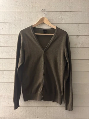 Olivgrön cardigan  - Stilren olivgrön cardigan från HM, tröjan har knäppning framtill. Tröjan är långa ärmad och har ribbade muddar vid ärmslut och nederkant. Perfekt att slänga över en t-shirt för en avslappnad look.