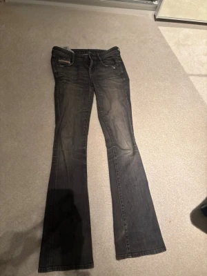 Mörkgrå bootcut jeans från diesel  - Säljer ett par mörkgrå bootcut jeans från diesel. Jeansen har låg midja och subtila detaljer vid fickorna. Perfekta för dig som gillar en avslappnad men trendig look.