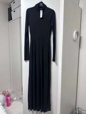 Svart poloklänning - lindex - En svart långklänning med lång ärm och polokrage. Klänningen har en enkel, stilren design och är gjord i ett mjukt, stretchigt material som sitter snyggt. Perfekt för dig som gillar minimalistisk stil. Nypris 399kr. 