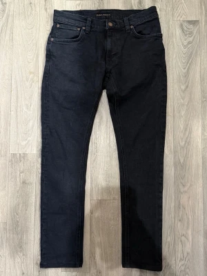 Nudie Jeans Svart W29/L32 - Skinny/Slim Fit - Mycket fint skick. Mått - Midja: 39cm, Ytterbenslängd: 95cm, Benöppning: 15cm. Modellen är 185cm & 63kg. Hör av dig vid funderingar!🤝