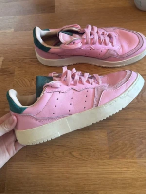 Adidas rosa sneakers med gröna detaljer - Snygga sneakers från Adidas i rosa läder med gröna detaljer på häl och plös. Använd en gång 