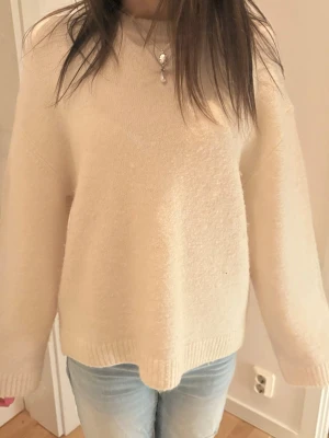 Beige oversized stickad tröja - Mysig beige stickad tröja med oversized passform och rund hals. Tröjan har långa ärmar och ribbade muddar vid ärmslut och nederkant. Perfekt att matcha med jeans för en avslappnad look.