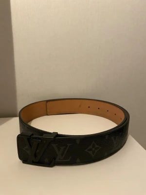 L,V bälte Helt Ny!!! - Snyggt svart skärp från  L,V bälte med klassiskt monogrammönster och stor L,V-logga i metall på spännet. Bältet är gjort i skinn med beige insida och har flera hål för justering. Perfekt accessoar för att lyfta din outfit.