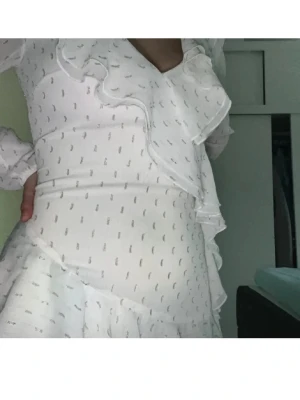 Studentklänning  - Säljer en söt vit klänning med volanger och diskret mönster. Klänningen har långa ärmar och en v-ringad design. Perfekt för en stilren look och perfekt för studenten!
