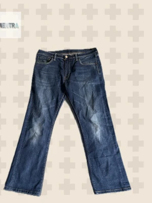 Blå bootcut jeans från Levi's - Säljer ett par klassiska blå bootcut jeans från Levi's med snygga slitningar på framsidan och fem fickor. Jeansen har en normal midja och är tillverkade i denim med typisk Levi's-lapp på bakfickan. Perfekt för dig som gillar en avslappnad och tidlös look.measurements +-1cmWaist 47cm inseam:78