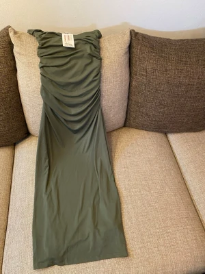Grön långklänning  - Snygg grön långklänning från New Yorker med åtsittande passform och rynkade detaljer upptill. Klänningen är axelbandslös och har en stilren, enkel design som passar perfekt till sommarens alla tillfällen. Med prislapp, aldrig använd.