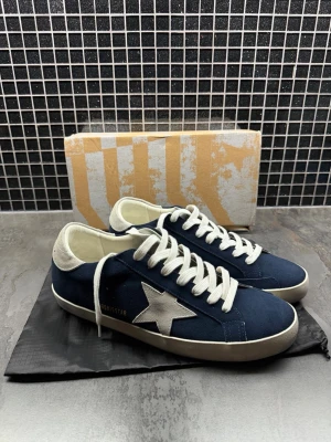 Mörkblå sneakers från Golden Goose - Snygga mörkblå sneakers från Golden Goose med vit stjärndetalj på sidan, vita skosnören och vit sula. Skorna har lågt skaft och kontrasterande vit häl. Tillverkade i mocka och textil för en cool och avslappnad look.