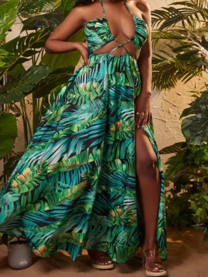 Grön långklänning med tropiskt mönster - Säljer en maxiklänning med tropiskt bladprint i gröna och blå toner. Klänningen har smala axelband, djup urringning, cut-out detaljer vid midjan och hög slits på ena sidan. Perfekt för sommarens varma dagar och semester. 