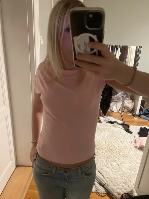 Ljusrosa kortärmad t-shirt - En enkel och stilren ljusrosa t-shirt med rund hals och korta ärmar. Passformen är normal och materialet känns mjukt, troligtvis bomull. Perfekt att matcha med jeans eller kjol för en avslappnad look.