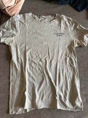Grå Calvin Klein Jeans t-shirt - Snygg grå t-shirt från Calvin Klein Jeans med diskret logga på bröstet. Klassisk rund halsringning och korta ärmar. Perfekt basplagg i mjuk bomull som passar till allt. Enkel och stilren design för en avslappnad look.