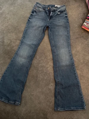 Blå bootcut jeans med utsvängda ben - Säljer ett par klassiska blå bootcut jeans med utsvängda ben och femficksmodell. Jeansen har en snygg tvätt med lätt slitning på låren och normalhög midja. Perfekta för dig som gillar retrostil och vill ha ett par jeans med skön passform. Har en liten sak på byxan men annars fin!