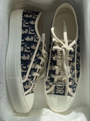 Christian Dior Oblique sneakers - Snygga låga sneakers från Christian Dior med det klassiska blå och beige Oblique-mönstret. Skorna har vita sulor, vit snörning och detaljer samt tydlig logga på sidan och tån. Tillverkade i canvas med gummisula för en trendig och exklusiv look.