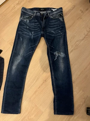 Mörkblå slitna jeans från Replay - Snygga mörkblå jeans från Replay med slitningar och distressed detaljer på både fram- och baksida. Klassisk femficksmodell med raka ben och tydliga kontrastsömmar. Jeansen har en cool tvätt och är tillverkade i denim.