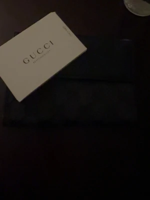 Svart plånbok från Gucci - Snygg svart plånbok från Gucci i canvas med det klassiska GG-mönstret över hela ytan. Plånboken har en stilren och tidlös design som passar perfekt i fickan eller väskan. Kommer med originalkort från Gucci.