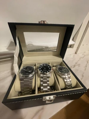 Set med tre silverfärgade klockor - Säljer ett set med tre stilrena armbandsur i silverfärgat metallarmband. Alla har svart urtavla, en med tydliga vita siffror och en med dag- och datumvisning. Perfekt för dig som gillar klassisk och clean stil. klockan åt höger. Har slut på batteri. men igår att fixa på en Klock-butik