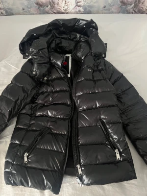 Svart pufferjacka från Tommy Hilfiger - Säljer en svart, glansig pufferjacka från Tommy Hilfiger! Pris går att diskuteras vid snabbt köp💞Knappt andvänd pga jag ville köpa en vit istället, finns med en päls till huvan som går å ta av och på om man skulle velat ha det. 
