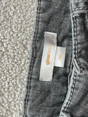 Grå jeans med broderade bakfickor - Säljer ett par grå low waist bootcut jeans med snygga broderade detaljer på bakfickorna. Jeansen är i storlek 140 men är uppsydda så att det passar någon som är ca 135 cm lång 