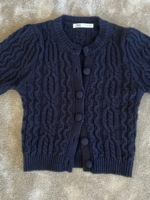 Mörkblå kabelstickad kofta från Zara - Jättesnygg mörkblå kabelstickad kofta från Zara med rund halsringning och stora tygklädda knappar. Bra skick, inte använd så mycket.