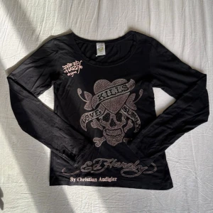Vintage Ed Hardy "Love Kills Slowly" Long Sleeve – Y2K Rhinestones - Säljer nu min autentiska långärmade Ed Hardy-tröja av Christian Audigier med det klassiska "Love Kills Slowly"-motivet. Toppen är täckt i gnistrande rhinestones, och även om det fattas några enstaka stenar (syns på bild)  är helhetsintrycket fortfarande riktigt snyggt. Enligt lappen är det storlek L, men den är liten i storleken och passar snarare en S eller M. Ett perfekt vintagefynd för dig som vill ha den rätta 00-talsstilen! Priset är diskuterbart & ni är välkomna att buda 