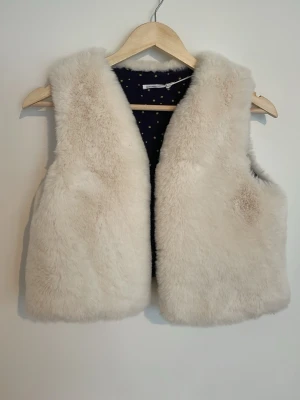 Pälsväst - Mysig och fluffig pälsväst i krämvit färg med ett mörkblått foder dekorerat med små stjärnor. Västen har en klassisk rak passform. Materialet är mjukt och fint❣️