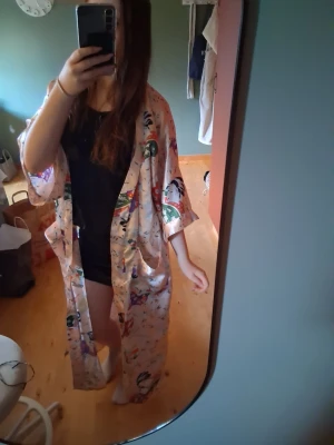 Lång kimono morgonrock med mönster - Säljer en lång, lös morgonrock i kimono-stil med färgglatt asiatiskt inspirerat mönster på ljus botten. Morgonrocken har vida ärmar och knytband i midjan. Perfekt för chill dagar hemma. Bandet fattas!💕