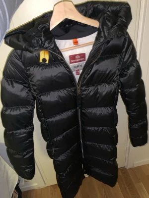 Svart lång dunjacka Parajumpers - Snygg svart lång dunjacka från Parajumpers, modell Sheen. Köpt på kidsbrandstore (kvitto finns) storleken är xs/s. Säljer pga det inte riktigt är min stil längre och använder den väldigt sällan. 