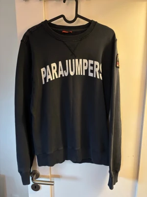 Mörkblå sweatshirt från Parajumpers - Snygg mörkblå sweatshirt från Parajumpers med stor vit logga framtill och patch på ärmen. Tröjan har rund hals, ribbade muddar och är tillverkad i mjukt bomullsmaterial. Perfekt för en avslappnad och trendig stil.