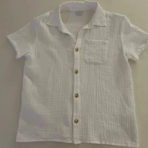 Vit linne skjorta - Luftig vit skjorta i mjuk bomull med klassisk krage, bröstficka och snygga knappar framtill. Skjortan har lång ärm och en avslappnad passform, perfekt för en stilren och enkel look.