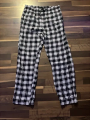 Rutiga pyjamasbyxor i svart och vitt - Mysiga pyjamasbyxor med svartvitt rutmönster och rak passform från Lager 157. Byxorna har resår i midjan och är perfekta för chill hemma. Materialet ser ut att vara mjukt och bekvämt, troligen bomull eller flanell.