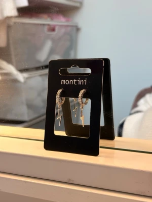 Silverörhängen med blixtar - Säljer ett par silvriga örhängen från ur & Penn  med små gnistrande stenar på ringen och hängande blixtberlocker. Örhängena har en modern och edgy look, perfekta för att lyfta vilken outfit som helst. Materialet är metall med stenar för extra bling.