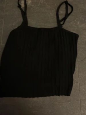Svart ribbad linnetopp - Säljer en svart ribbad linnetopp med smala axelband. Toppen är croppad och har en enkel, stilren look som passar perfekt till jeans eller kjol. Perfekt för dig som gillar minimalistisk stil.