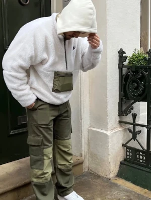 Vit fleece-tröja från Nike - Säljer en vit, mysig fleece-tröja från Nike med halv dragkedja och en grön ficka framtill. Tröjan har en avslappnad passform och broderad Nike-logga på bröstet. Perfekt för lager-på-lager och streetwear-stil.