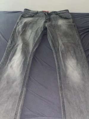 Grå jeans från Plus 8 Denim - Snygga grå jeans från Plus 8 Denim med slitna detaljer och klassisk femficksmodell. Jeansen har raka ben och tydliga sömmar, perfekt för en avslappnad och trendig look. Materialet är denim i bomull med en cool tvättad finish.