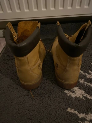 Beige Timberland boots i läder - Klassiska beige boots från Timberland i robust läder med bruna detaljer och vadderad svart krage. Grov sula för bra grepp och snörning med metallhål. Perfekta för dig som vill ha en tidlös och street-inspirerad look.