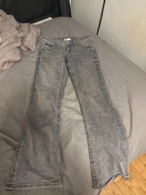 Grå bootcut jeans med dubbla knappar - Säljer ett par grå bootcut jeans med cool tvätt och dubbla knappar i midjan. Jeansen har klassiska fickor fram och bak samt en extra liten ficka. Materialet är denim och passformen är lite utsvängd nertill.