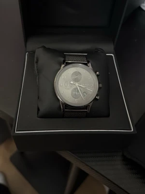 Stilren klocka från Hugo Boss - Snygg klocka från Hugo Boss med svart mesh-armband i rostfritt stål och silverfärgad urtavla. Klockan har tre subdials, datumvisning och tydliga siffror. Perfekt accessoar för dig som gillar en modern och elegant look.