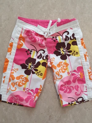 Shorts - Säljer ett par färgglada shorts med blommigt mönster i rosa, orange, gul, brun och vitt. Shortsen har snörning i midjan och en bakficka med dragkedja.