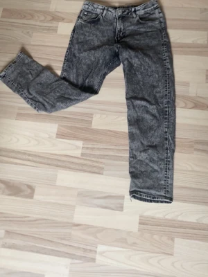 Gråa jeans - Säljer ett par grå tvättade jeans med rak passform och klassisk femficksdesign. Jeansen har en cool, lite sliten look och är perfekta för en avslappnad stil. Materialet är troligtvis bomull med en mjuk känsla. Passar dig som gillar vintage vibe.