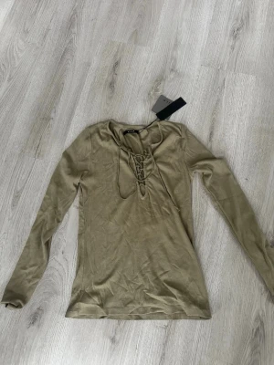 Grön långärmad topp med snörning - Snygg grön  långärmad topp från VILA med trendig snörning framtill. Modellen är figurnära och har en mjuk, stretchig känsla som passar perfekt till jeans eller kjol. Enkel men ändå med en cool detalj framtill. Pris lapp finns kvar. Nypris är 250kr