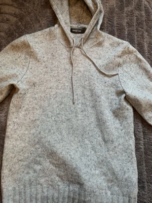 Ljusgrå hoodie från Dressmann - Mysig ljusgrå hoodie från Dressmann med huva och dragsnören. Tillverkad i mjukt stickat material som känns skönt mot huden. Klassisk modell med ribbade muddar vid ärmslut och nederkant. Perfekt för en avslappnad och stilren look.