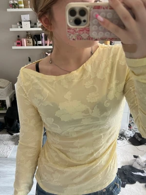 Ljusgul blommig mesh topp - Säljer en ljusgul långärmad mesh topp med blommigt mönster. Toppen är tight och har en lätt transparent känsla, perfekt för att styla lager på lager. Superfin till jeans eller kjol!