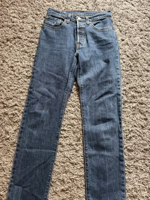 Blå raka jeans från Levi's - Klassiska blå jeans från Levi's med rak passform och fem fickor. Jeansen har en tidlös look med kontrastsömmar och knappgylf. Tillverkade i slitstark denim som passar perfekt till en avslappnad stil. Storlek 26/30. Fler bilder kan skickas, vid visat intresse🙂